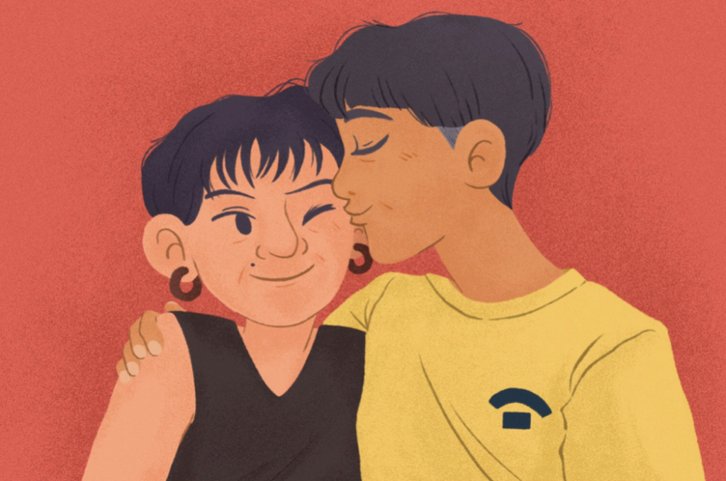 An image of two short-haired women—the taller one in a yellow t-shirt giving a kiss to the shorter one with a mole by her mouth.